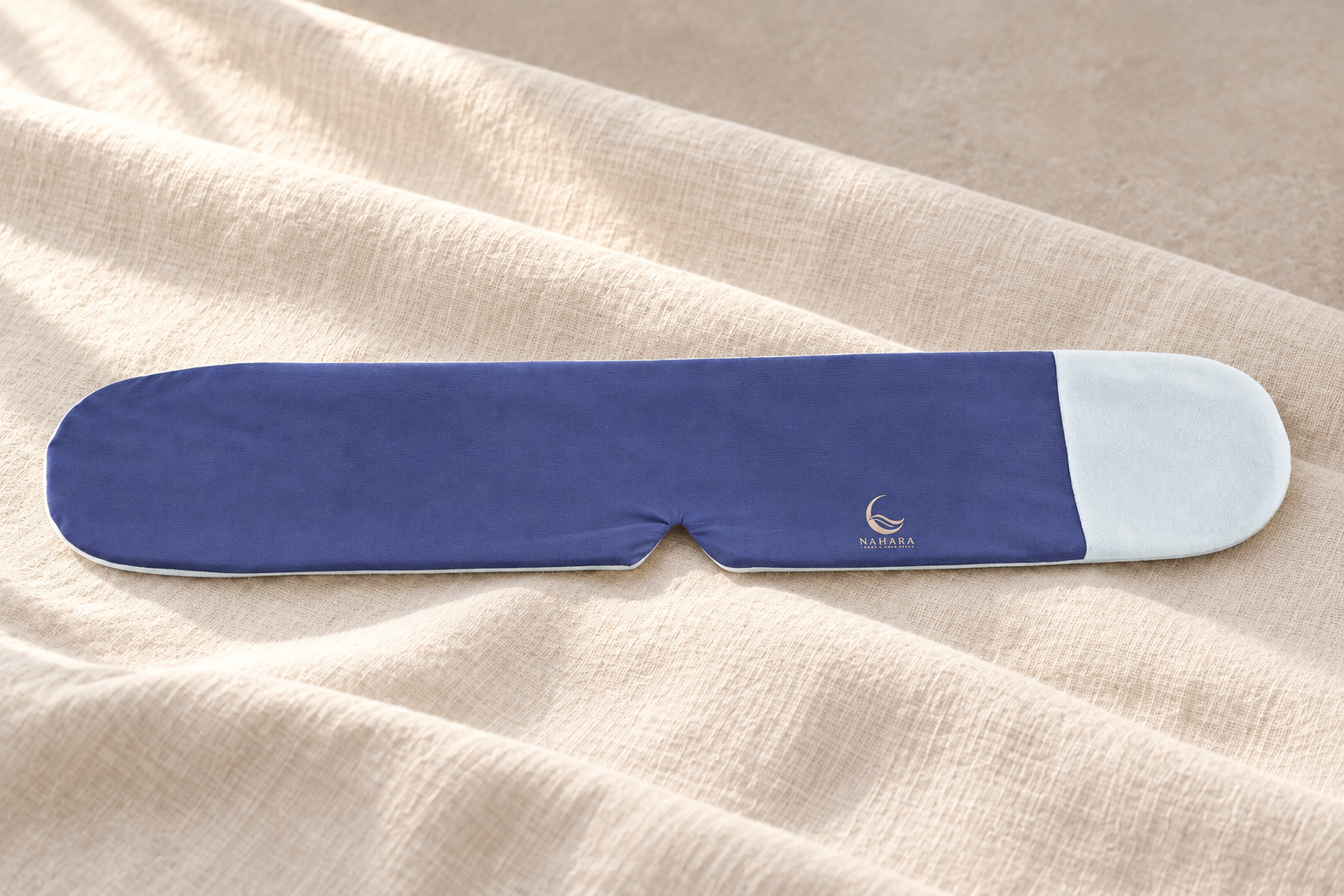 NAHARA indigo and pale-blue weighted eye mask with gold branding and fine fabric detail, arranged on softly draped ivory linen